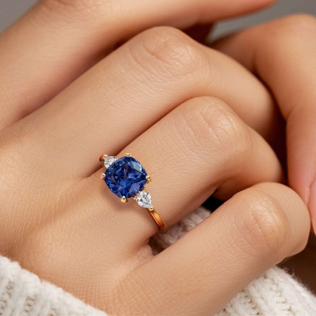 Woman wearing a cushion cut 3 stone ring with romantic styling featuring blue sapphire and diamonds.