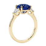 Three stone cushion diamond ring in yellow gold setting with blue sapphire and diamonds.