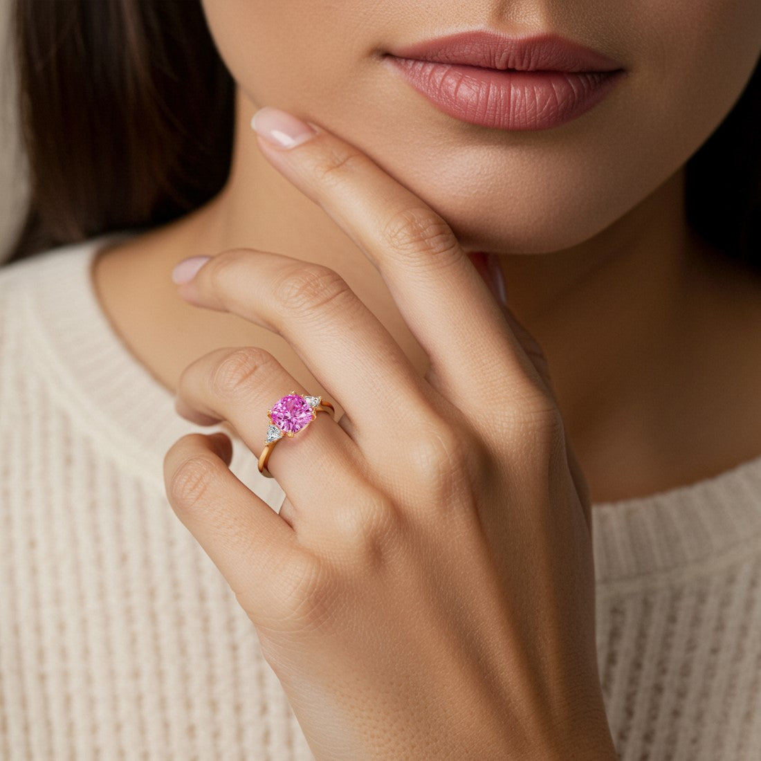 Woman wearing a cushion cut 3 stone ring with romantic styling featuring pink sapphire and diamonds.