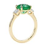 Three stone cushion diamond ring in yellow gold setting with green gemstone and diamonds.