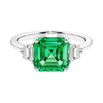 Asscher gemstone diamond ring with step-cut sparkle in a three stone setting featuring colombian emerald center.