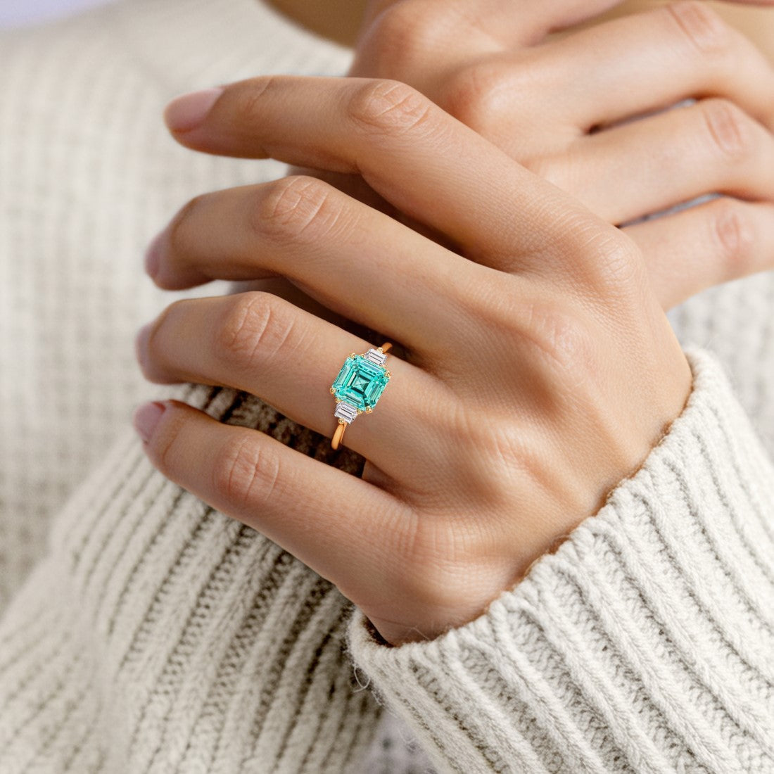 Woman wearing a 3 stone Asscher engagement ring with vintage flair featuring a paraiba tourmaline center.