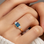 Woman modeling a princess cut three stone engagement ring with alexandrite and diamonds.