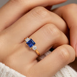 Woman modeling a princess cut three stone engagement ring with blue sapphire and diamonds.