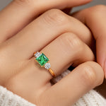 Woman modeling a princess cut three stone engagement ring with colombian emerald and diamonds.