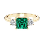 Princess cut 3 stone engagement ring with side diamonds and emerald gemstone center.