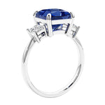 Engagement ring with princess cut diamonds in a 3 stone design featuring blue sapphire gemstone center.
