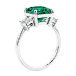 Engagement ring with princess cut diamonds in a 3 stone design featuring green emerald gemstone center.