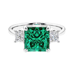 3 stone princess diamond ring in sleek white gold with green emerald gemstone center.