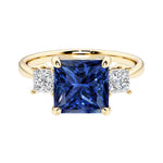 Princess cut 3 stone engagement ring with square side diamonds and blue sapphire gemstone center.