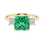 Princess cut 3 stone engagement ring with square side diamonds and colombian emerald gemstone center.