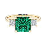 Princess cut 3 stone engagement ring with square side diamonds and green emerald gemstone center.